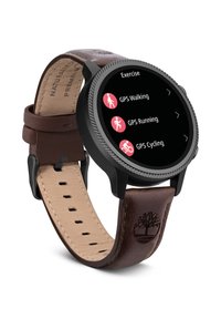 Ronde smartwatch met een zwarte metalen bezel en een zwart aanraakscherm dat trainingsopties weergeeft. Bruin lederen band met reliëflogo en stiksels.