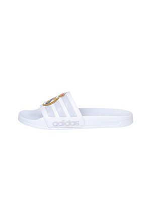 Sandalia tipo slide blanca de Adidas con tres rayas y un logo del Real Madrid en la correa, con el logotipo de Adidas en relieve en el lateral.