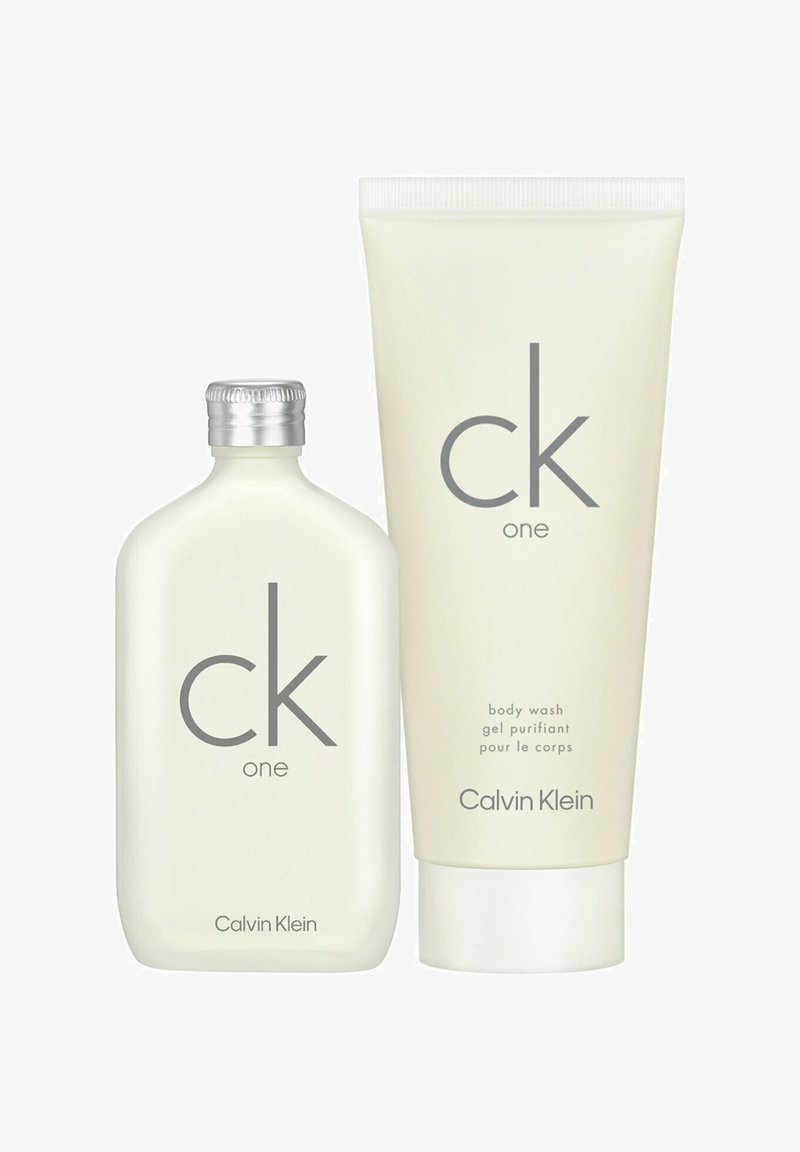Two CK One Calvin Klein products: a frosted glass bottle with silver cap and a cream-colored body wash tube. Both have minimalist gray text.