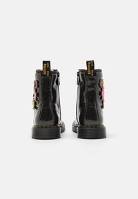 Bottes de cheville en cuir verni noir avec une finition pailletée, appliques florales en rose et vert sur le côté, et semelles en caoutchouc noir ; fermeture éclair.