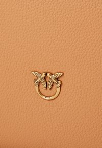 Persiku krāsas ādas rokassoma ar faktūras virsmu un zelta tonī gredzenu, uz kura attēlotas divas izsmalcināti veidotas putni, ar zīmolu "PINKO".