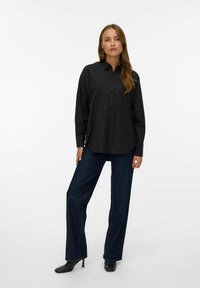 Camicia nera a bottoni con vestibilità ampia, decorata con applicazioni a pallini argentati. Abbinata a jeans a gamba larga blu scuro e stivaletti neri con tacco.