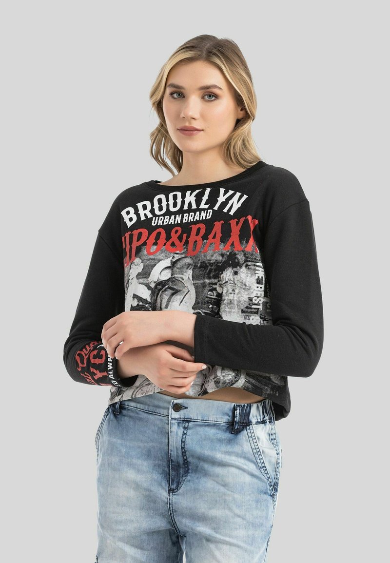 Schwarzes Langarmshirt mit Grafikdruck, auf dem "BROOKLYN" in Weiß und Rot steht, kombiniert mit hellblauen Denim-Shorts.