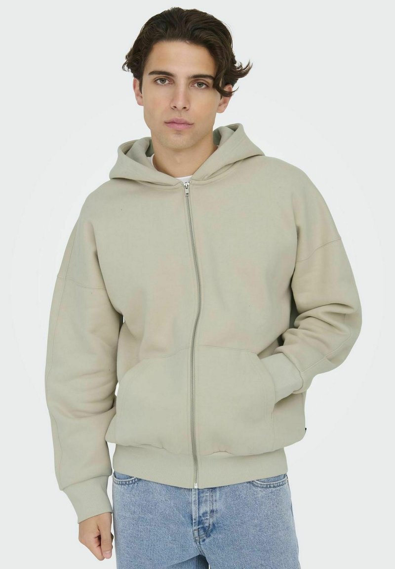 Lichtgrijze zip-up hoodie met een trekkoordcapuchon, voorzakken en geribbelde manchetten. Gladde textuur en ontspannen pasvorm.
