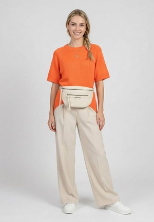 Young woman with blonde braid wearing an orange short-sleeve sweater, beige wide-leg pants, white sneakers, and a beige waist bag.