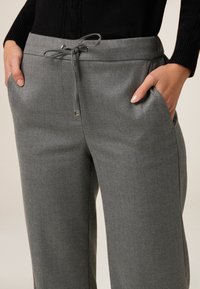 Pantalones grises con una textura suave, cierre de cordón y bolsillos laterales, con un sutil patrón de espiga.