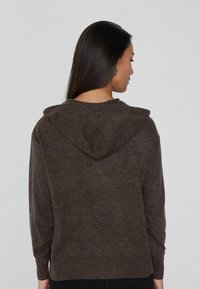 Sudadera con capucha de color marrón oscuro, fabricada con material suave, que presenta una gran capucha, mangas largas y puños y dobladillo acanalados. Textura suave.