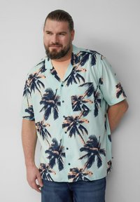 Korte mouwen knop-up blouse, mintgroen met donker marineblauwe palmbomenprint, zakdetail, lichte stof, relaxte pasvorm, gecombineerd met blauwe jeans.