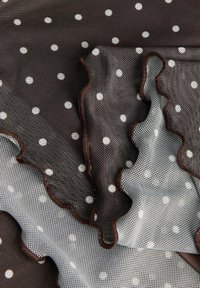 Tela de malla con Lunares marrones y blancos, con bordes ondulados y una textura translúcida en capas.