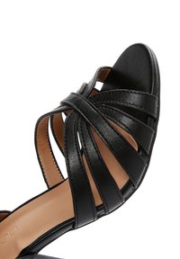 Sandalo nero con cinturini, caratterizzato da una suola piatta, texture in pelle, design open toe e più bande orizzontali sulla parte superiore.