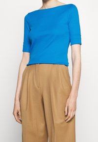 Top azul de manga corta con escote barco, hecho de una tela suave, combinado con pantalones de pierna ancha de cintura alta en color marrón claro.