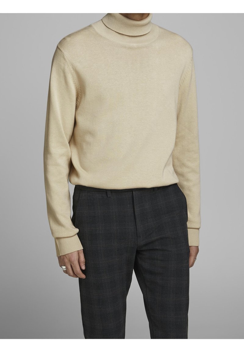 Beige polotröja gjord av mjukt material, med ribbade ärmslut. Kombinerad med mörka rutiga byxor med ett subtilt rutmönster.