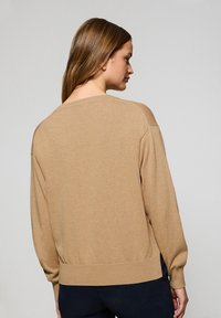 Lysbrun sweater med en afslappet pasform, ribbede manchetter og kantdetaljer samt en bred halsudskæring. Stoffet ser blødt og struktureret ud.