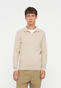 Beige geribbelde longsleeve polo trui met een kraaghals, voorzien van een gestructureerd oppervlak en een getailleerde pasvorm.