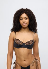 Μαύρο σουτιέν με δαντέλα πάνω μέρος σε λευκόχρυση λεοπάρ εκτύπωση, με λεπτομέρειες βολάν και λεπτές τιράντες. Το υλικό είναι λείο με ματ υφή.