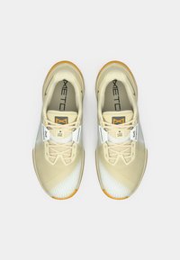 Μπεζ αθλητικά παπούτσια με υφή στην επάνω πλευρά, λευκές λεπτομέρειες και πορτοκαλί καουτσούκ σόλες. Περιλαμβάνει κορδόνια και επένδυση στον λαιμό για στήριξη.