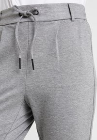 Šedé joggingové kalhoty vyrobené z měkké, strukturované tkaniny. Disponují elastickým pasem se stahovací šňůrkou a bočními kapsami. Pohodlný střih.