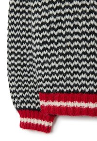 Suéter de punto con un patrón de zigzag en blanco y negro, con puños a rayas rojas y crema, hecho de lana suave. Detalle de tejido texturizado visible.