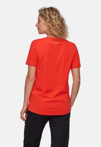 Röd kortärmad t-shirt med avslappnad passform, med en vit logga på baksidan och rundad halsringning. Tillverkad av mjukt bomullstyg.