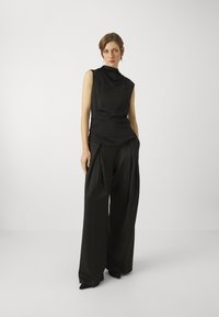 Černý bezramínkový top s draped límcem, v kombinaci s širokými černými kalhotami s záhyby. Hladká struktura a minimalistický design.