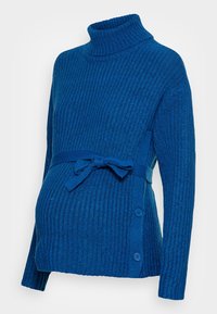 Pull de maternité en maille côtelée bleue avec un col roulé haut, une ceinture à nouer à la taille et des boutons sur le côté. Texture douce et coupe décontractée.
