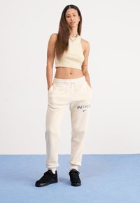 Top crop canelado em bege claro combinado com calças de fato brancas largas com um logótipo cinza da Nike, complementado por ténis pretos.