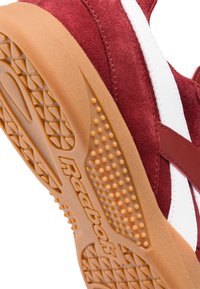 Červené semišové tenisky s bílými koženými akcenty a gumovou podrážkou s texturovaným gripem, na boku s logem "Reebok".