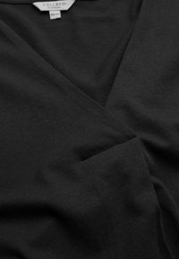 Zwarte, zachte katoenen t-shirt met een V-hals ontwerp, subtiele textuur en een diagonale naaddetail. Label leest "CELLBES uit Zweden."