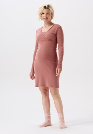 Langwerpige, roze jurk met een crossoverhalslijn en aansluitend lijfje. Zachte, ribbelige textuur. Model draagt bijpassende roze sokken.