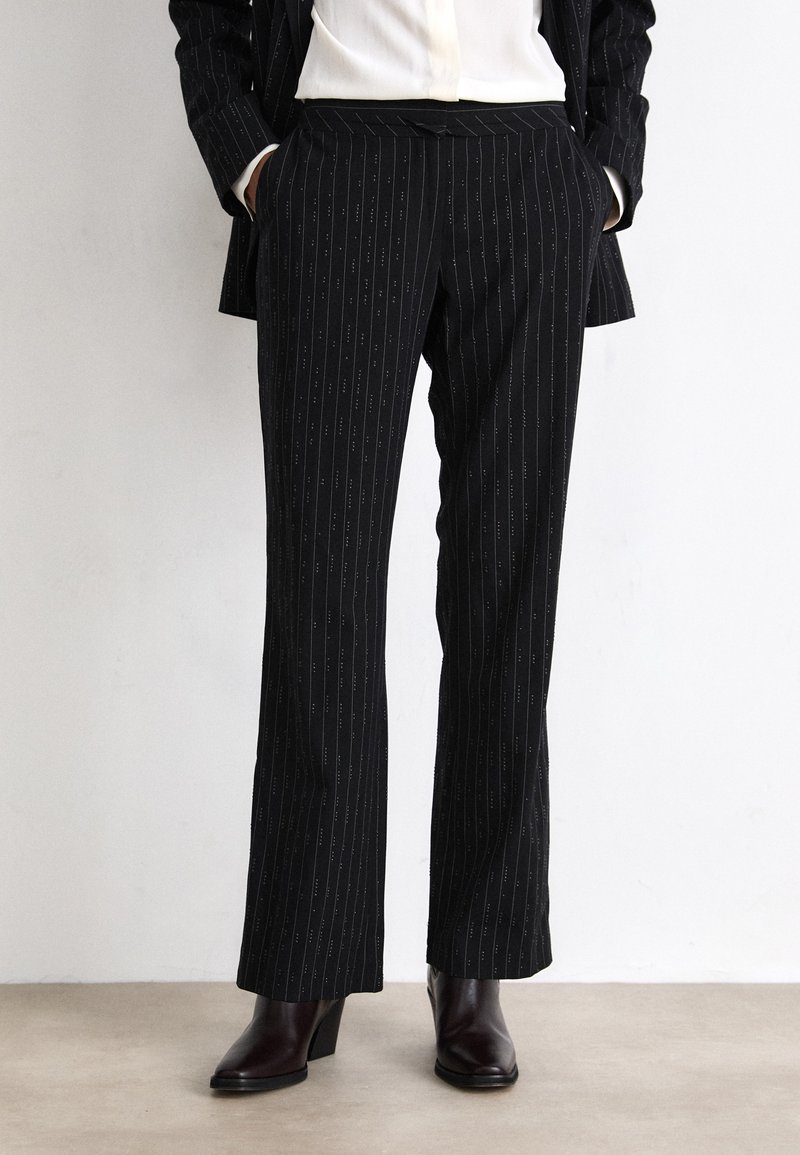 Pantalon noir à rayures fines, à coupe slim, avec une taille plate, des poches latérales, fabriqué en tissu lisse ; associé à des bottines.