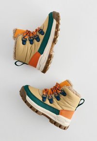 Tansfarbene wasserdichte Stiefel mit orangefarbenen und grünen Akzenten, strukturiertem Kunstfellfutter, ausgeprägter profilierter Sohle und kontrastierenden Schnürsenkeln.