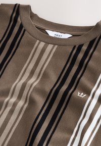 Barna csíkos pulóver környakú nyakkivágással, bézs, fekete és fehér vízszintes csíkokkal, és egy kis fehér logóval a mellkason.