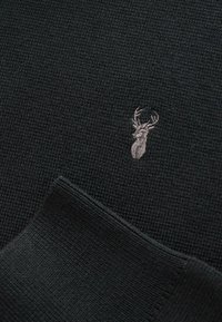 Maglione nero lavorato a maglia con una texture a coste e un discreto logo di un cervo ricamato in grigio sul petto. Design semplice e pulito.