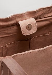 Intérieur de sac fourre-tout en daim rose avec une fermeture à pression, comprenant plusieurs poches et une texture lisse le long des bords.