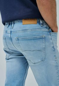 Jeans de mezclilla azul claro con un diseño ajustado, que cuentan con una etiqueta de cuero marrón en la cintura y costuras de bolsillo en colores contrastantes.