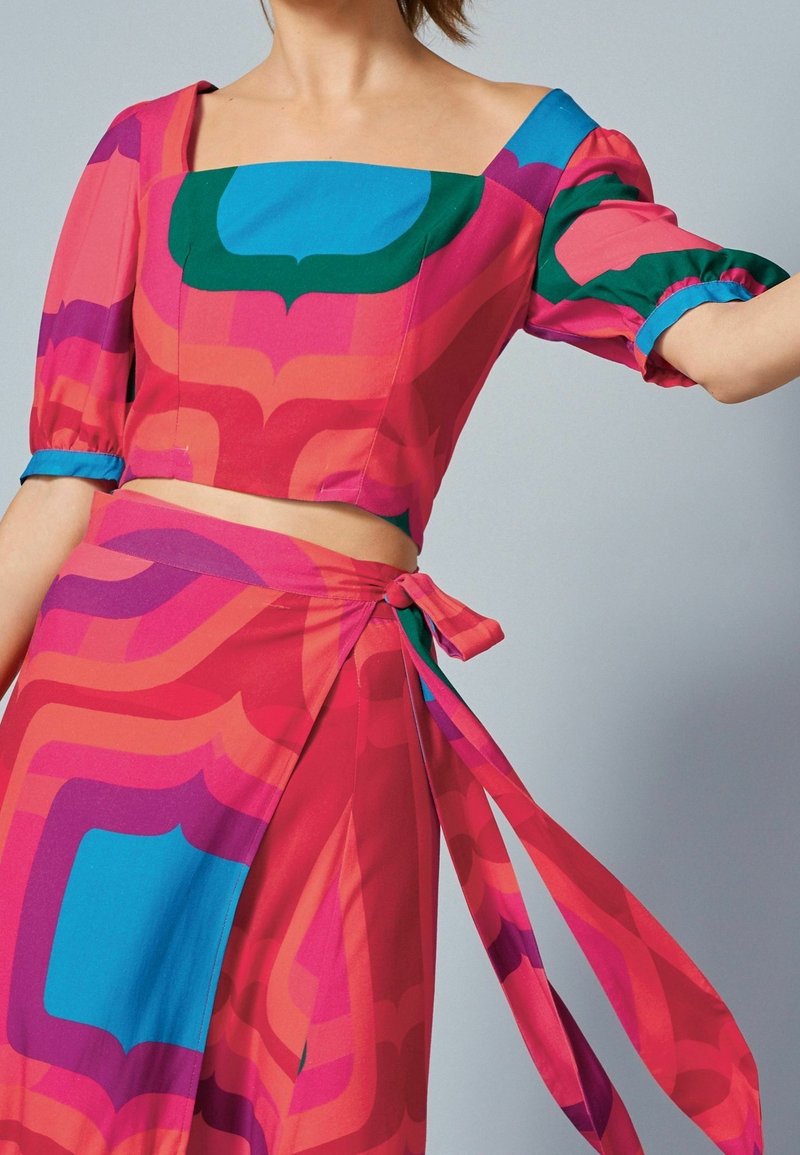 Crop top og omslagskørt sæt i livlige pink, blå og grønne abstrakte mønstre, med puffede ærmer og sidesnøringsdetaljer.