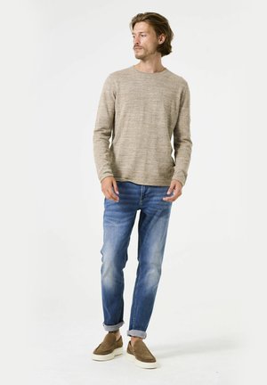 Hellbraunes Strickpullover mit Rundhalsausschnitt, kombiniert mit hellblauen Jeans und braunen Slippern, in lässiger Passform und mit aufgerollten Ärmeln.