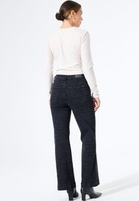 Zwarte, gepatterde flared jeans van denim, met een subtiele zebra-streep textuur, gecombineerd met een lichtgekleurde getailleerde top en enkellaarsjes.