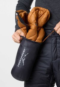 Svart packbar dunjacka med brunt innerfoder, vikta i sin förvaringspåse som har en logotyp och snörningsstängning.