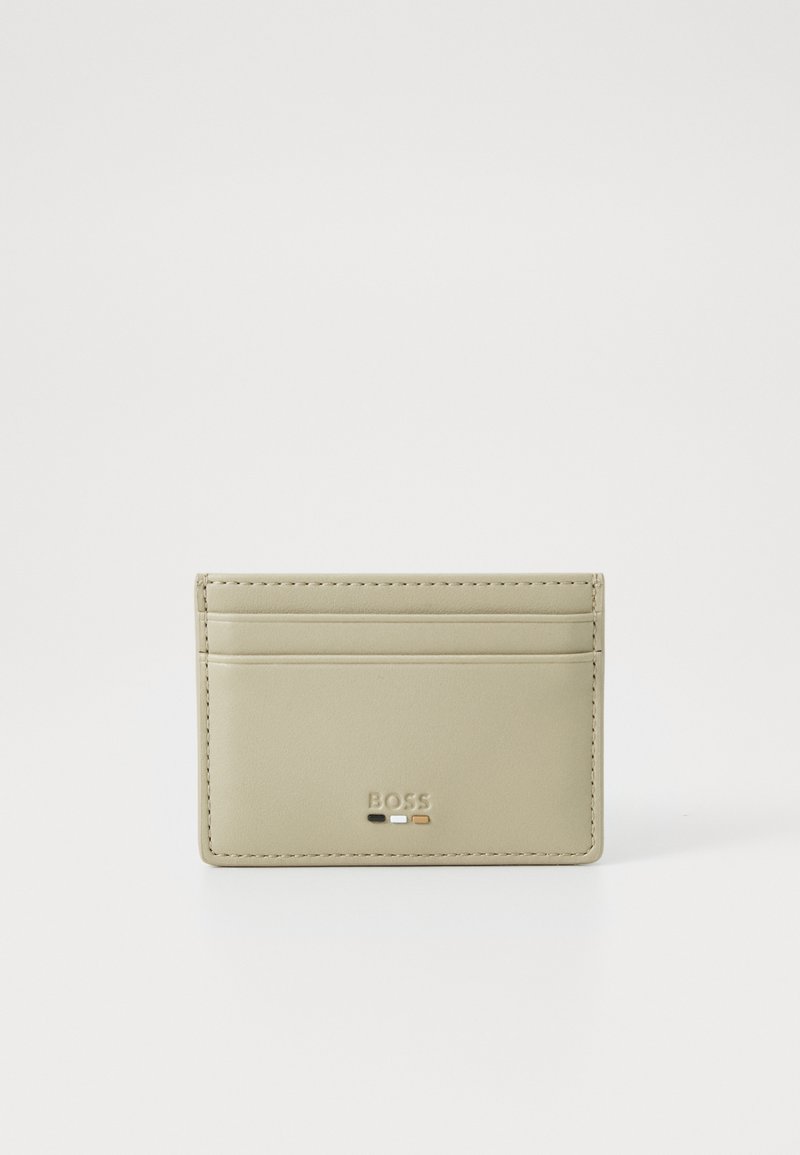 Portafoglio in pelle di un beige chiaro con quattro slot per carte, logo in rilievo e dettagli di cucitura discreti. Texture liscia e design minimale.