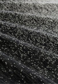 Primo piano di un tessuto a maglia nero e grigio con una sottile trama a macchie e pieghe morbide.