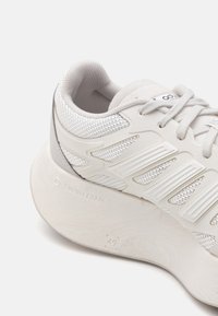 Hvite sneakers med overdel i mesh med teksturerte striper, en polstret såle merket "SWIRLFOAM", og et avrundet design.
