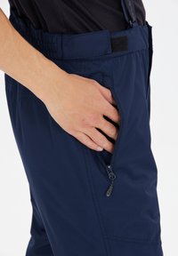 Marina vattentäta byxor med elastisk midja, som har en dragkedjeförsedd sidoficka och en slät, matt tygkänsla.