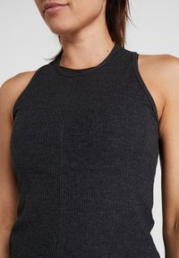 Musta ribattua topia, jossa on korkea kaula-aukko, hihaton muotoilu ja teksturoitu pinta. Tiukka leikkaus korostaa kehon muotoa.