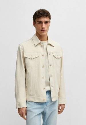 Crème denimjasje met een klassieke kraag, twee borstzakken, knoopsluitingen en een recht gesneden ontwerp. Draagt over een licht shirt.