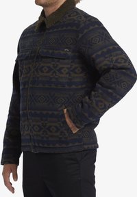 Fleece jacket featuring a dark navy base with geometric brown patterns, zip front, two chest pockets, and a textured green collar.