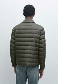 Olive green puffer jacket with quilted sections, a collar, and a smooth texture. Worn over light wash denim jeans.