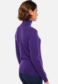 Pull en col roulé violet en maille douce, avec des manches longues, une silhouette ajustée et des accents côtelés au niveau du col et de l'ourlet.