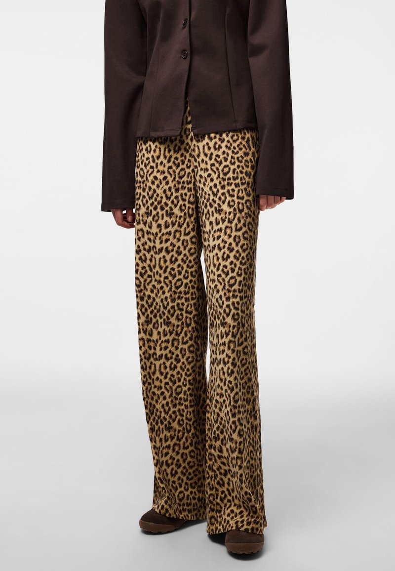 Vida byxor med leopardmönster i beige och svart, kombinerade med en brun figursydd jacka. Slät textur och avslappnad passform över hela.