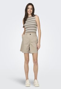 Pantaloni corti color khaki con chiusura a bottone e tasche laterali, abbinati a una maglietta senza maniche di colore verde oliva a righe orizzontali bianche.